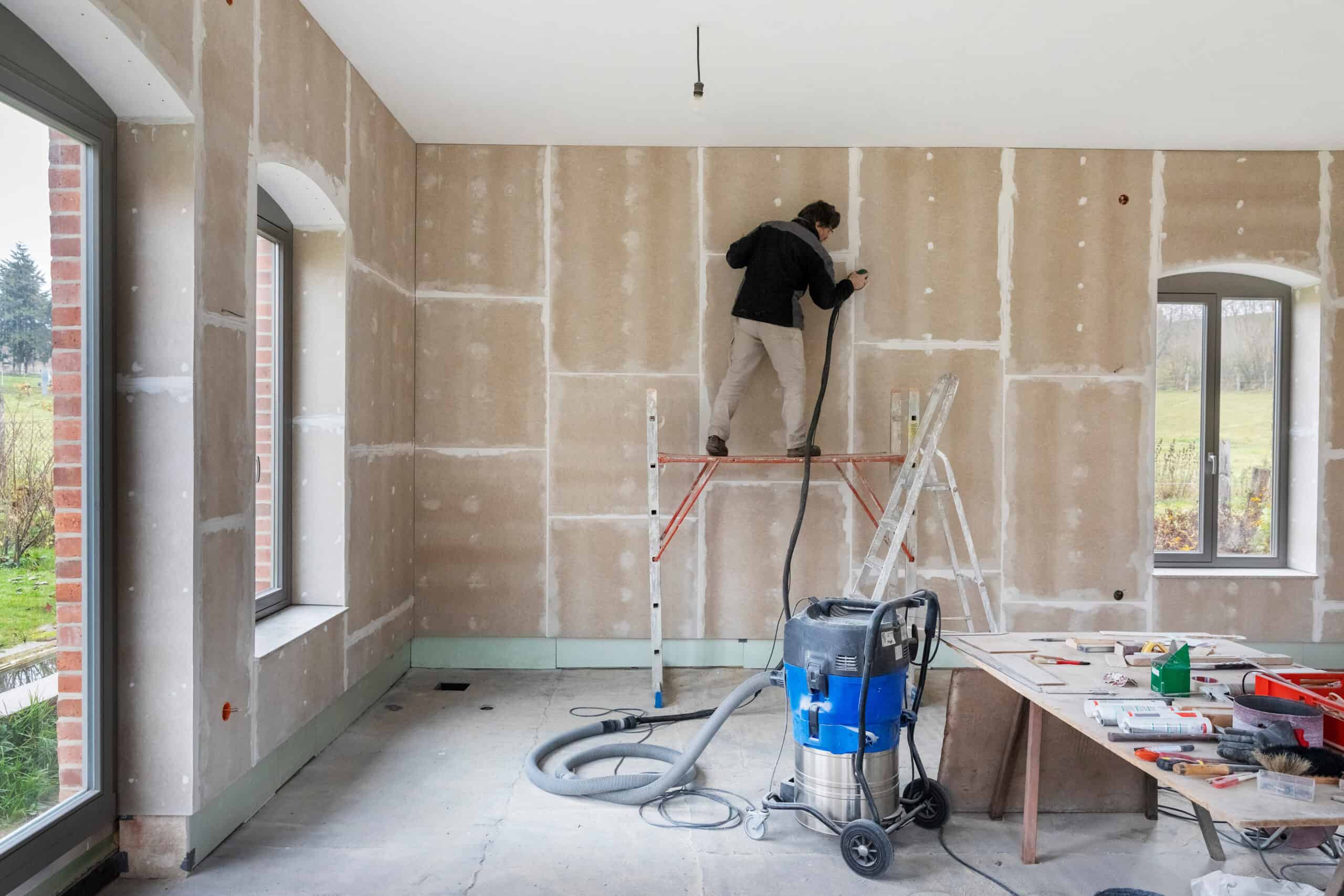 Innendämmung von Außenwänden – eine sinnvolle Alternative zur Fassadendämmung? Ein Mann auf einer Leiter, der einen Raum eines Haus mit einer Innendämmung ausstattet.